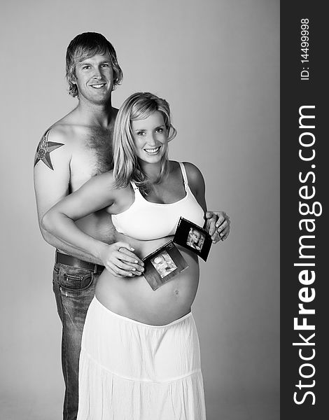 A young, pregnant woman is smiling as she stands in front of a man holding photographs of her ultrasound. Vertical shot. A young, pregnant woman is smiling as she stands in front of a man holding photographs of her ultrasound. Vertical shot.