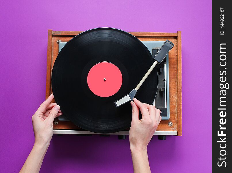 Female hands set up retro vinyl record player with plate on purple background. Top view