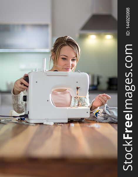 Pretty, young woman sewing clothes with sewing machine color toned image; shallow DOF