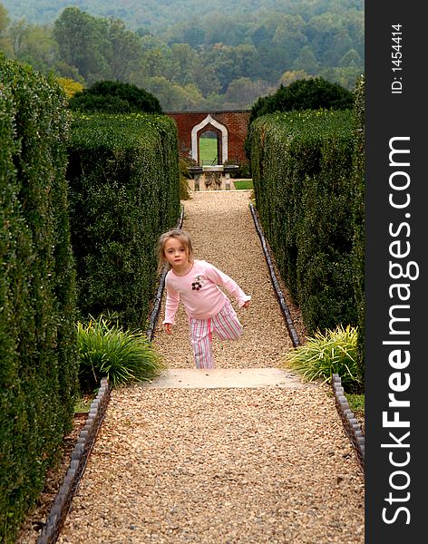 A little girl hopping, skipping and jumping on a path in the garden with a view in the background. A little girl hopping, skipping and jumping on a path in the garden with a view in the background.