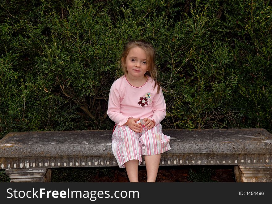 A beautiful little girl dressed in pink sitting on a concrete garden bench. She's wearing flip-flops and has a sweet expression on her face. A beautiful little girl dressed in pink sitting on a concrete garden bench. She's wearing flip-flops and has a sweet expression on her face.