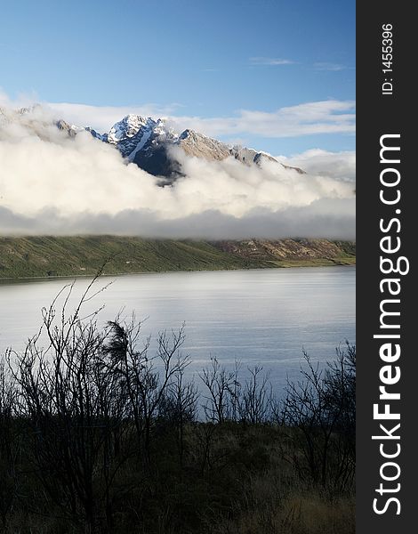 Cloudy snow mountain and lake at New Zealand, framed with dry trees. Cloudy snow mountain and lake at New Zealand, framed with dry trees.