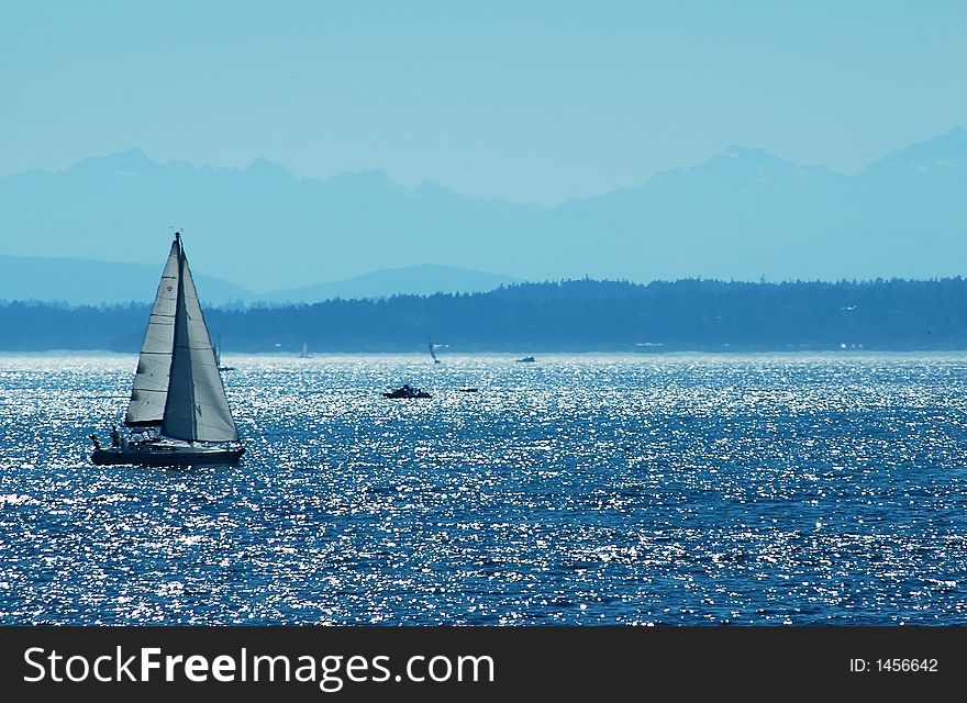 Sailboat on blue ocean water with mountain range in the distance. Sailboat on blue ocean water with mountain range in the distance