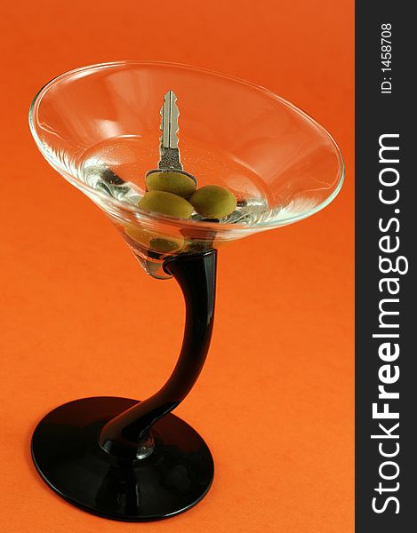 Martini with car keys inside against orange background - drinking and driving concept