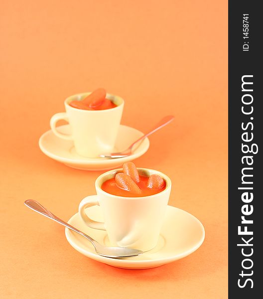 Baby carrots and juice presented in esspresso cup against orange background. Baby carrots and juice presented in esspresso cup against orange background