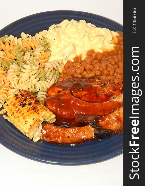 Spare ribs corn potato and pasta salad and baked beans on a dinner plate. Spare ribs corn potato and pasta salad and baked beans on a dinner plate