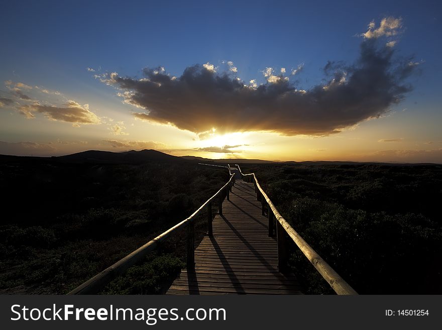 Image of a wooden walkway towards a sunset. Image of a wooden walkway towards a sunset