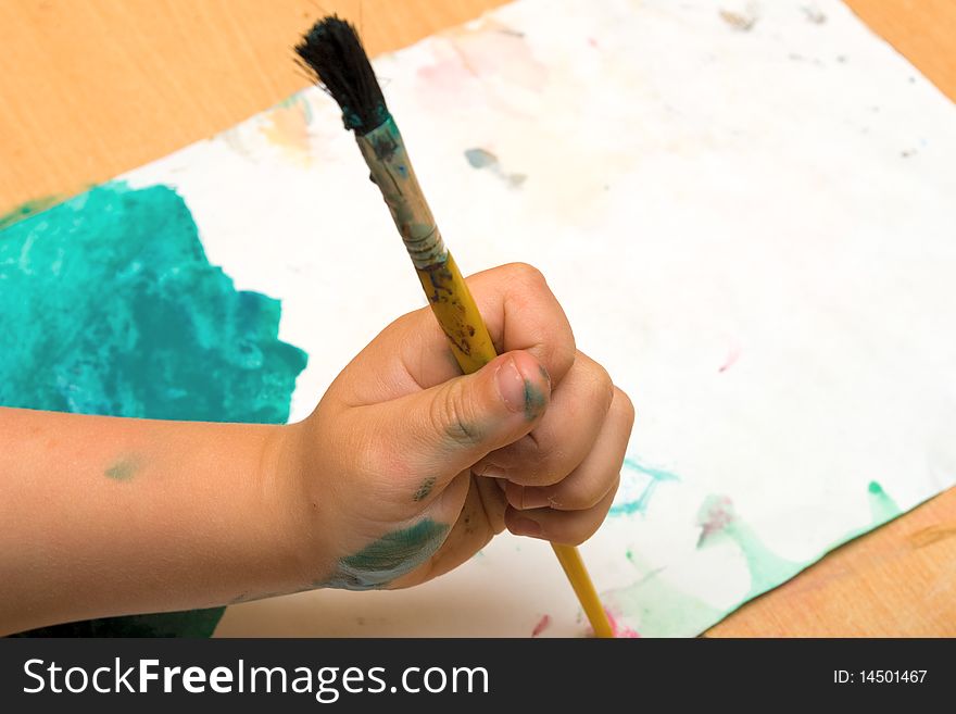 Child hand holding a brush on a watercolor paint. Child hand holding a brush on a watercolor paint