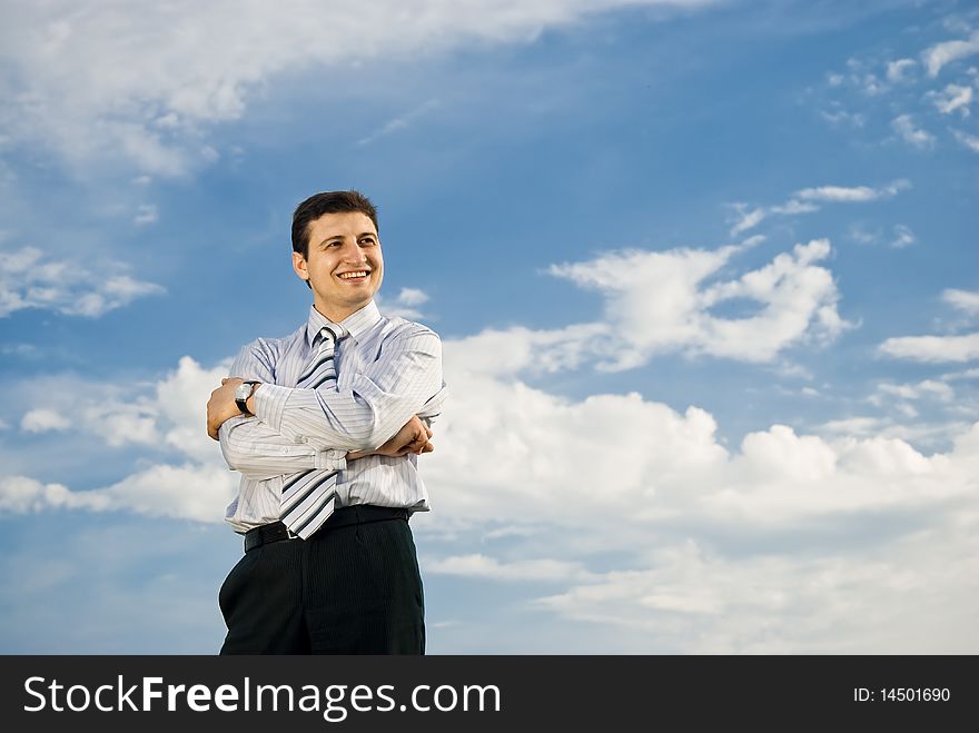 A young smiling businessman is staying outdoors on a very cloudy background