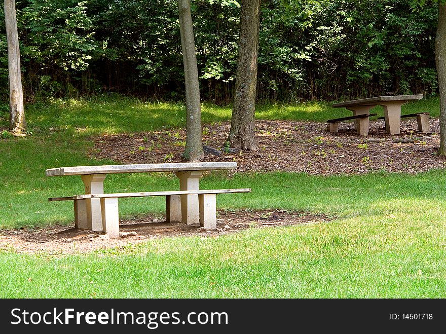 A pair of picnic tables in a wooded area of a public park.