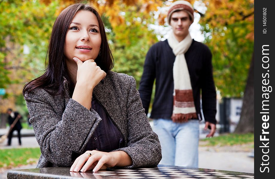 Young woman sitting in park, male coming from behind. Young woman sitting in park, male coming from behind