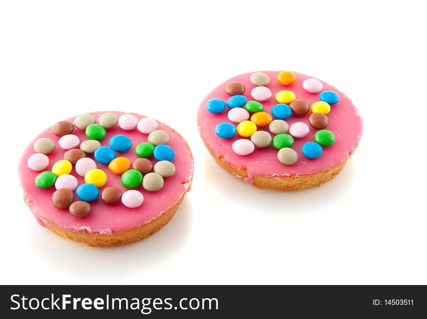 Two pink icing cakes  with colorful chocolate candy on top isolated over white