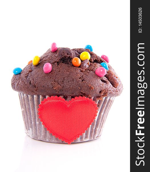 A lovely chocolate muffin with chocolate candy on top and a heart isolated over white