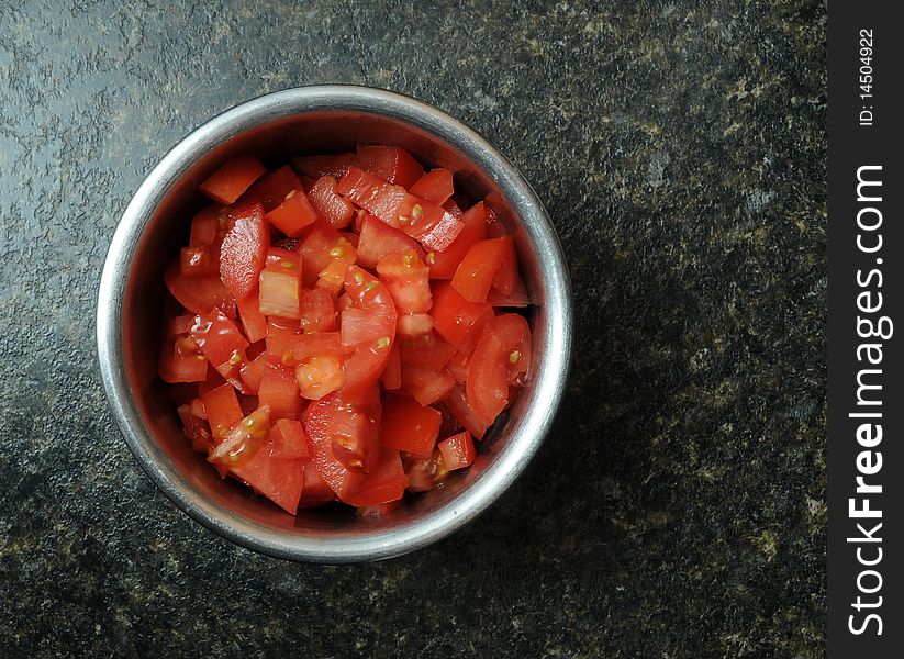 A bunch of sliced, diced, and cut red tomatoes inside of a round metal bowl resting on a kitchen counter top. A bunch of sliced, diced, and cut red tomatoes inside of a round metal bowl resting on a kitchen counter top