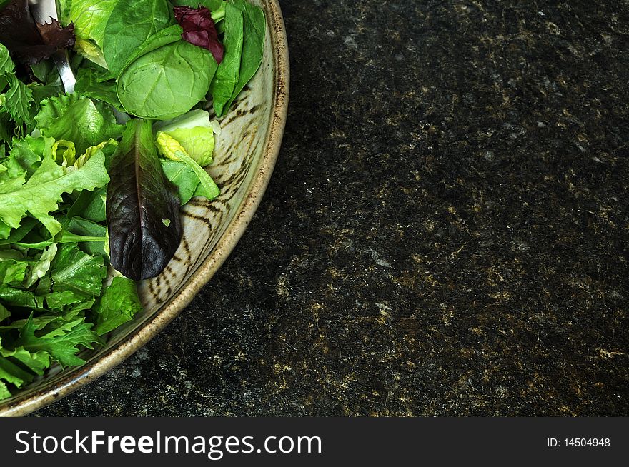 A variety of green lettuce tossed in a salad bowl, sitting on a black kitchen counter top. Copyspace on the right. A variety of green lettuce tossed in a salad bowl, sitting on a black kitchen counter top. Copyspace on the right.