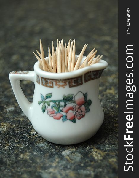 A bunch of toothpicks contained in a miniature tea glass resting on a black counter top with shallow depth of field