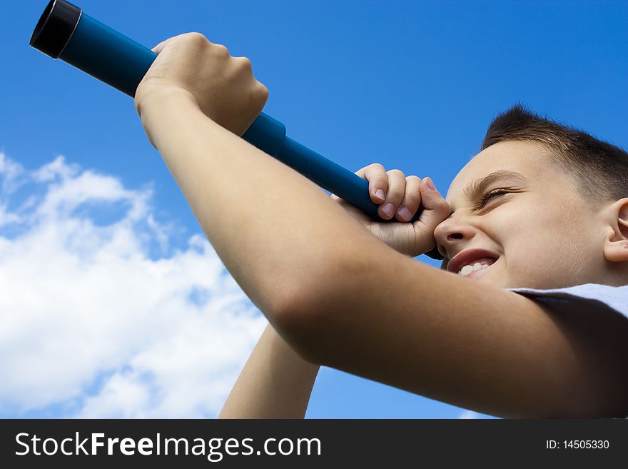 The boy looks through a telescope while standing on the green field on a background of blue sky