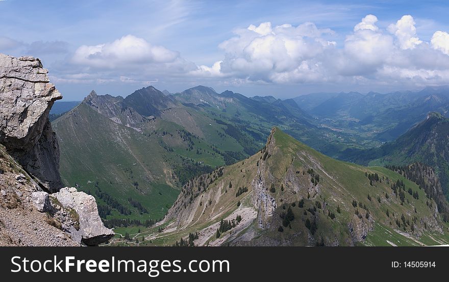 A panoramic view on rocky mountains under clouds with green slopes. Alpes, Switzerland, Europe. A panoramic view on rocky mountains under clouds with green slopes. Alpes, Switzerland, Europe.