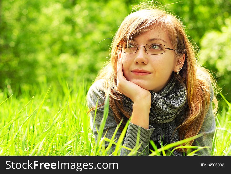 The young girl, in glasses, lays on a green grass, in park. The young girl, in glasses, lays on a green grass, in park