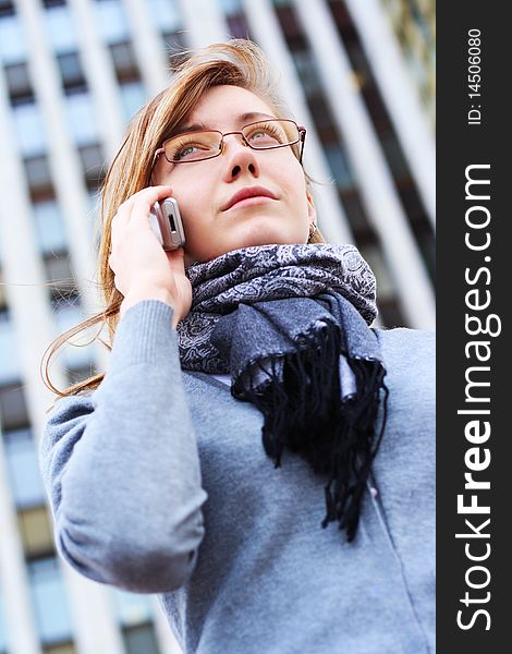 The business young girl with speaks by phone, on a background of a city building. The business young girl with speaks by phone, on a background of a city building