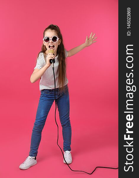 Cute girl singing in microphone on color