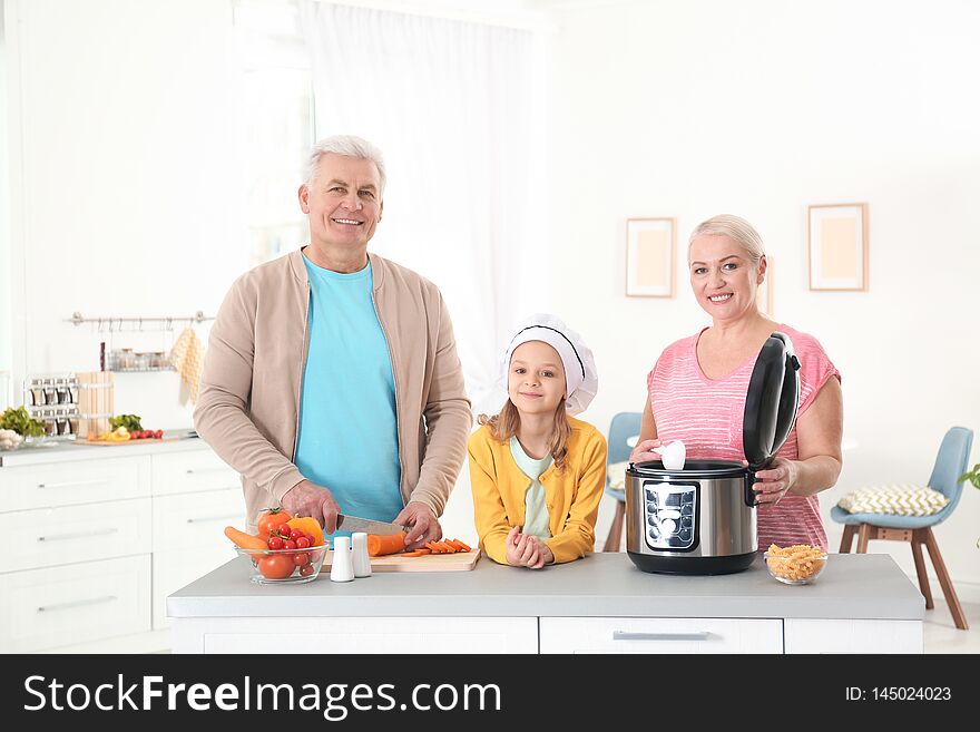 Mature couple and their granddaughter preparing food with modern multi cooker