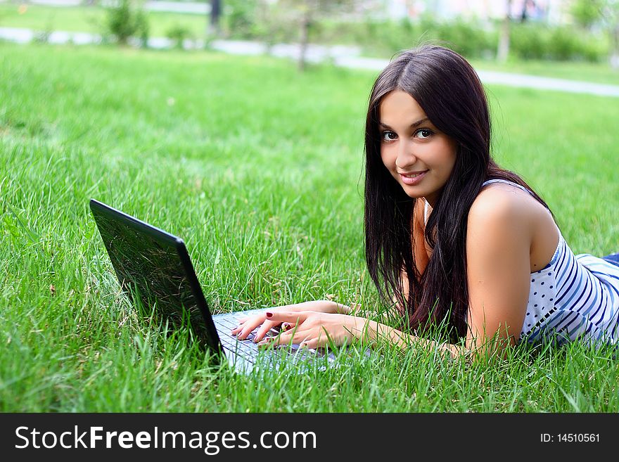 Young woman with laptop lying jn the green grass
