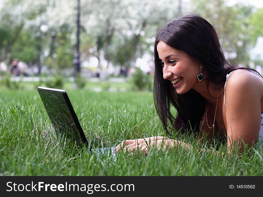 Young woman with laptop lying jn the green grass