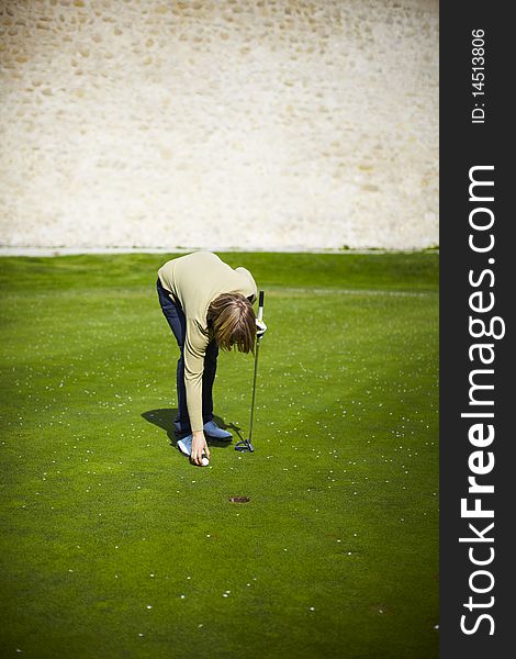 Woman at the golf range preparing golf ball and stone wall on a background.