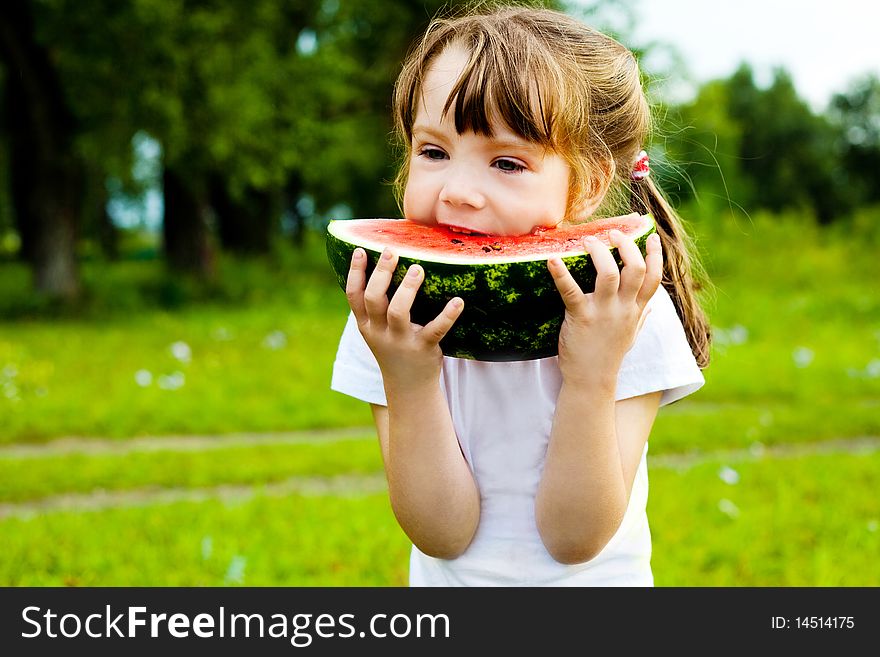 Cute little girl eating watermelon on the grass in summertime
