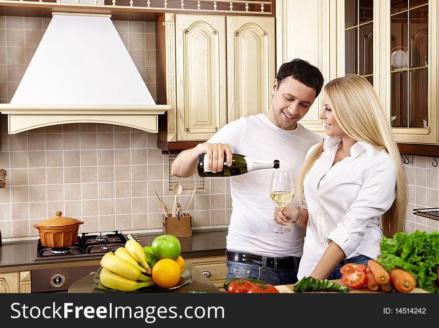 The young man pours champagne to the girl on kitchen. The young man pours champagne to the girl on kitchen