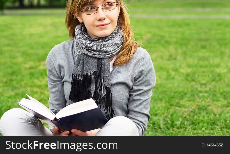 The young girl in glasses, sits on a grass and reads the book. The young girl in glasses, sits on a grass and reads the book