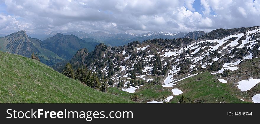 A panoramic view on rocky mountains under clouds with green slopes. Alpes, Switzerland, Europe. A panoramic view on rocky mountains under clouds with green slopes. Alpes, Switzerland, Europe.