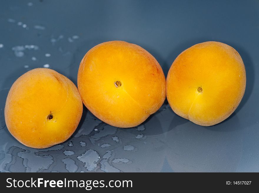 Three wet peaches on a blue table in the rain