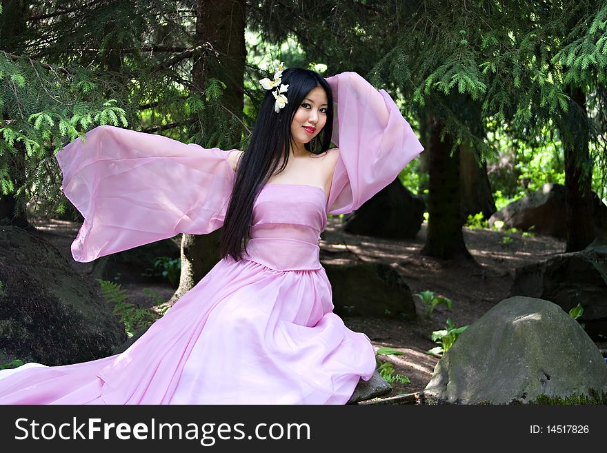 Beutiful japanese woman in pink dress sitting on the stone near the spring