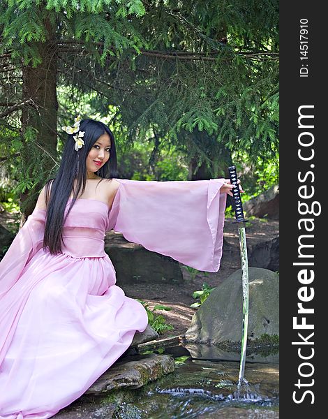 Beutiful japanese woman in pink dress sitting on the stone wields a katana