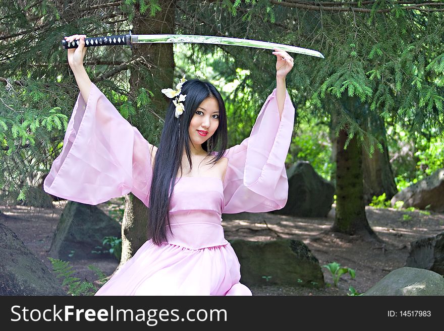 Beutiful japanese woman in pink dress sitting on the stone wields a katana
