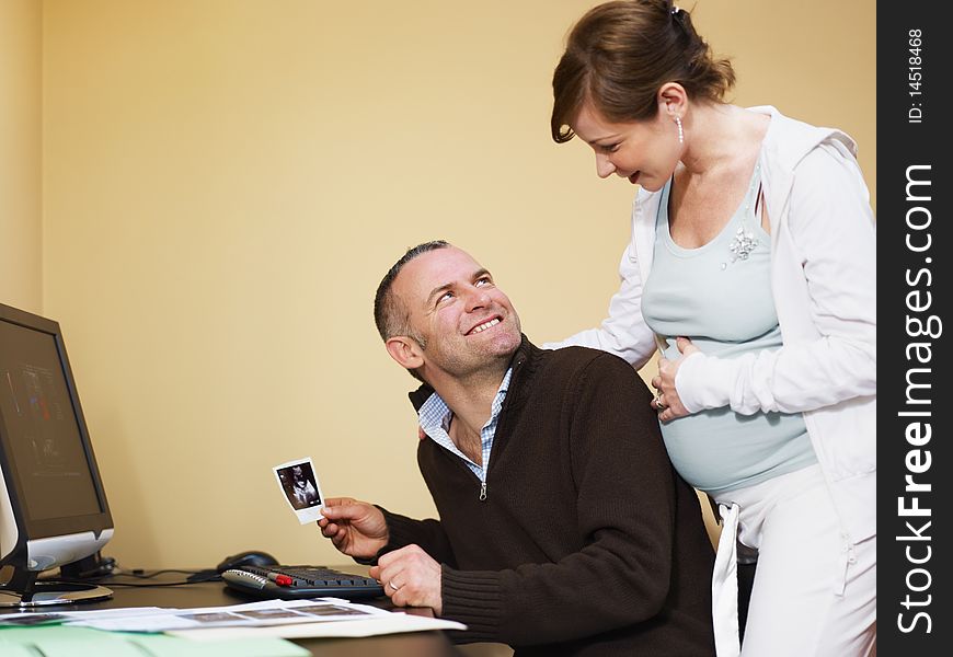 Italian 6 months pregnant woman and her husband watching ultrasound pictures of her baby on desktop computer at home. Horizontal shape, side view, copy space. Italian 6 months pregnant woman and her husband watching ultrasound pictures of her baby on desktop computer at home. Horizontal shape, side view, copy space