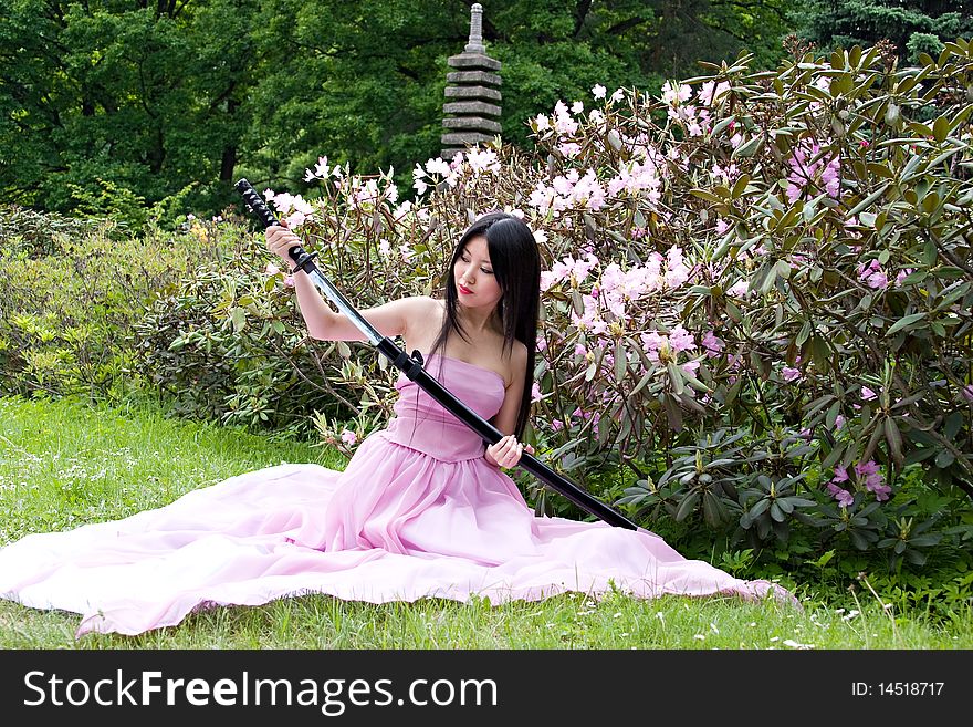 Beautiful asian woman in a pink dress sitting on the ground with a sword in the hands. Beautiful asian woman in a pink dress sitting on the ground with a sword in the hands