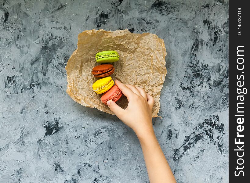 Tasty colorful fresh macaroons and hand child on gray table. Tasty colorful fresh macaroons and hand child on gray table