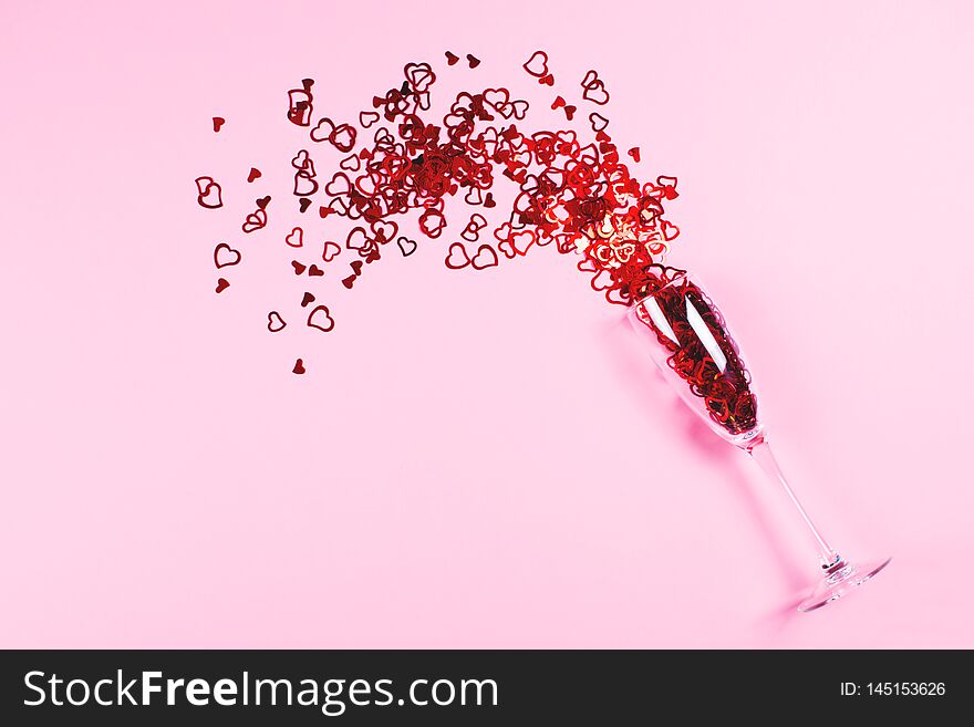 Heart-shaped vibrant red confetti poured out of champagne glass on pink background with copy space for text. Top view and flat lay style. Holiday, love and celebration concept. Heart-shaped vibrant red confetti poured out of champagne glass on pink background with copy space for text. Top view and flat lay style. Holiday, love and celebration concept