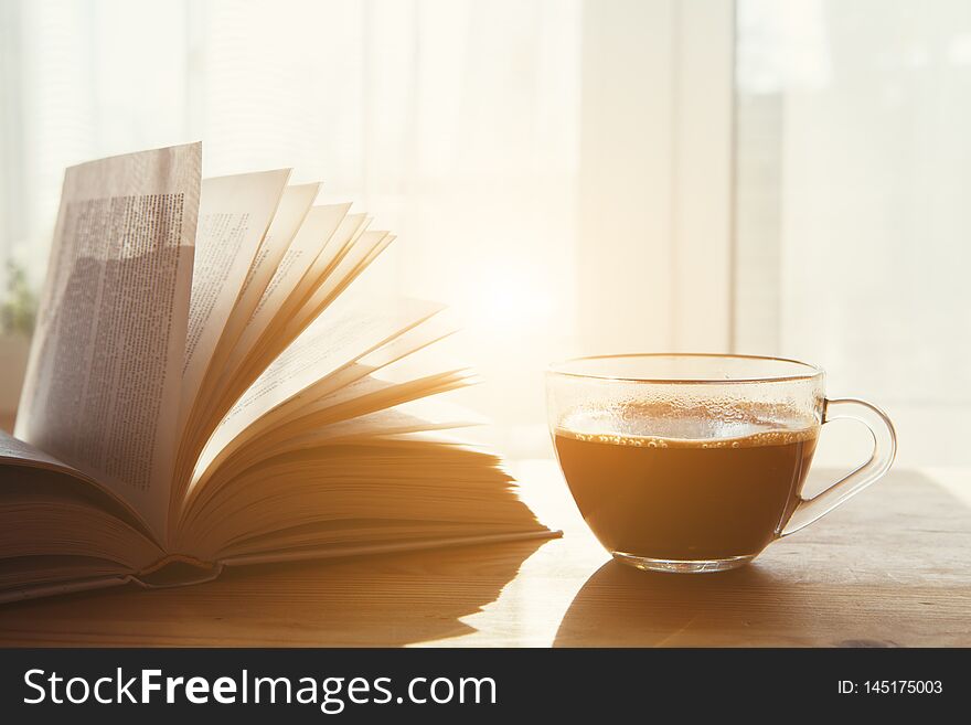 Cup of morning coffee and open book on wooden table