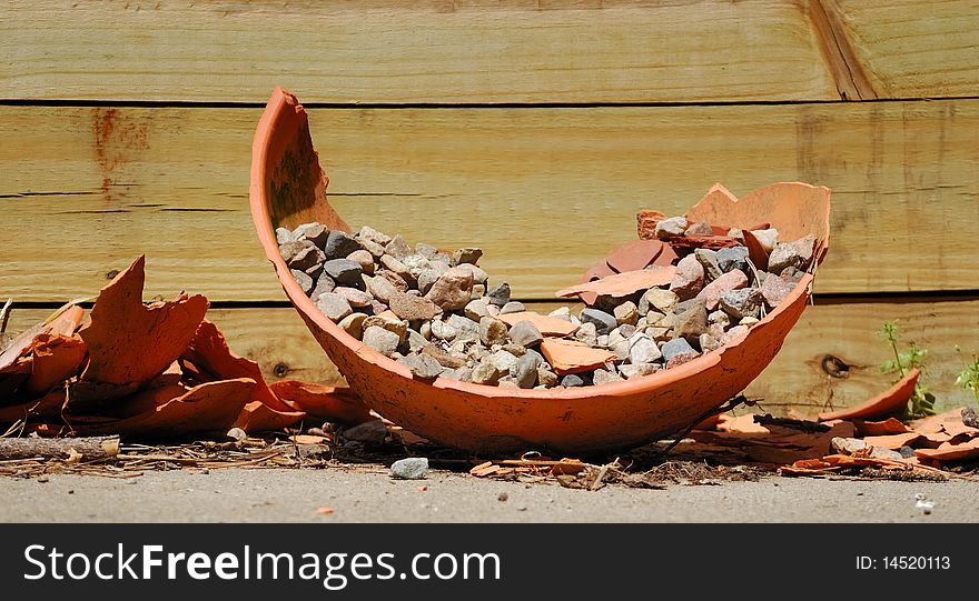 Broken flower pot discarded next to wooden retaining wall. Broken flower pot discarded next to wooden retaining wall