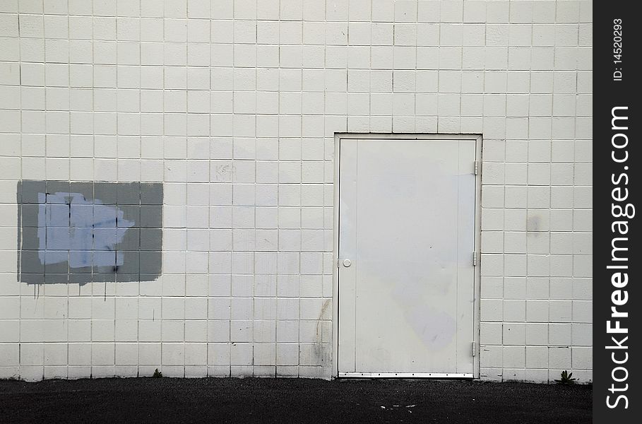 Tiled wall with a blank white door and gray spray paint covering graffiti. Tiled wall with a blank white door and gray spray paint covering graffiti.