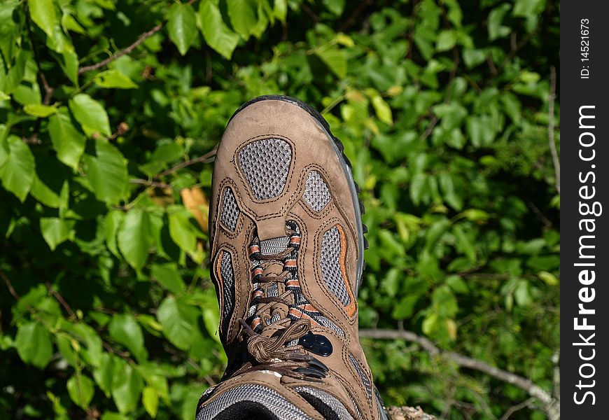 One foot hanging on the edge of mountain side.  A brown hiking boot. One foot hanging on the edge of mountain side.  A brown hiking boot.