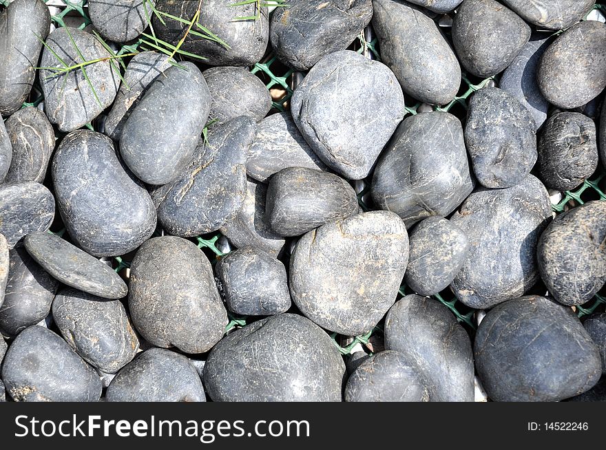 Detail of a typical cobblestone as background on the road with little green plastic grass. Detail of a typical cobblestone as background on the road with little green plastic grass