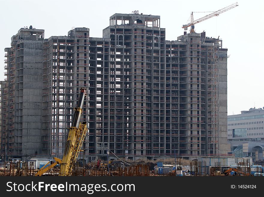 Building crane at the background of a multi-storey building under construction