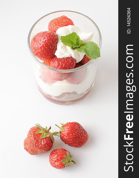 Strawberries with whipped cream and mint leaf in a glass on a white background