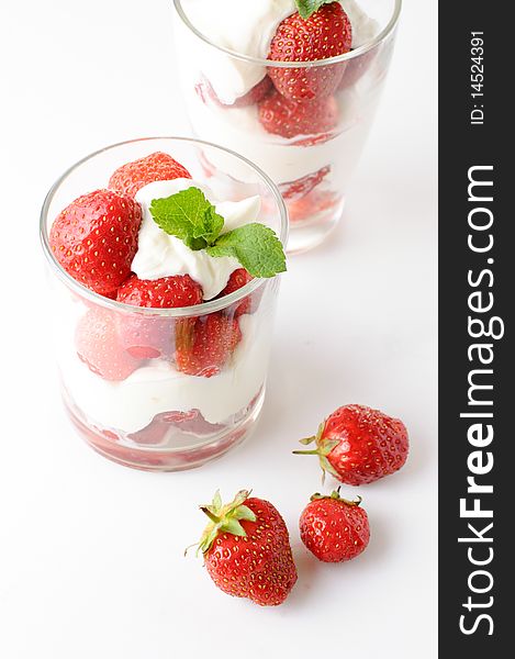 Two cups with strawberry dessert with a mint leaf on a white background