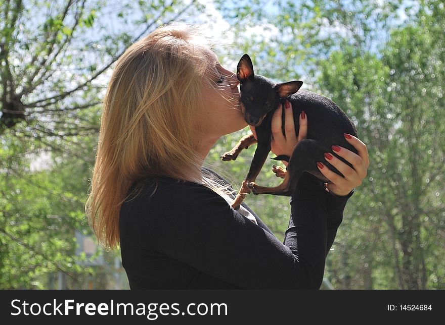 Blond girl with small black dog in hands. Blond girl with small black dog in hands